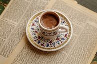Elegant coffee cup with intricate designs on vintage newspaper background, offering a traditional and cultural feel.