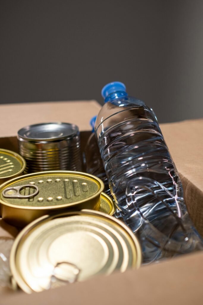 Collection of canned goods and plastic water bottle in a cardboard box for emergency preparedness.