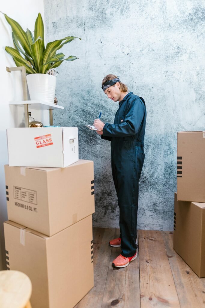 A Caucasian mover in coveralls packing and organizing cardboard boxes indoors.
