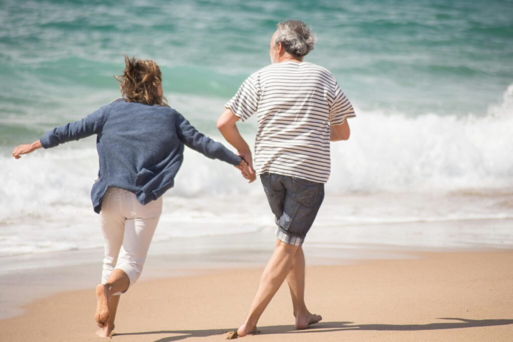 Senior couple holding hands and running by the ocean at a Portuguese beach during the day.