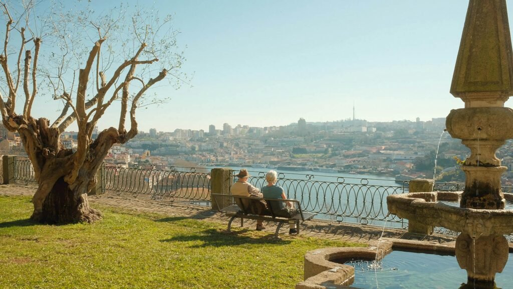 A serene scene of an elderly couple on a bench overlooking Porto's river and cityscape.